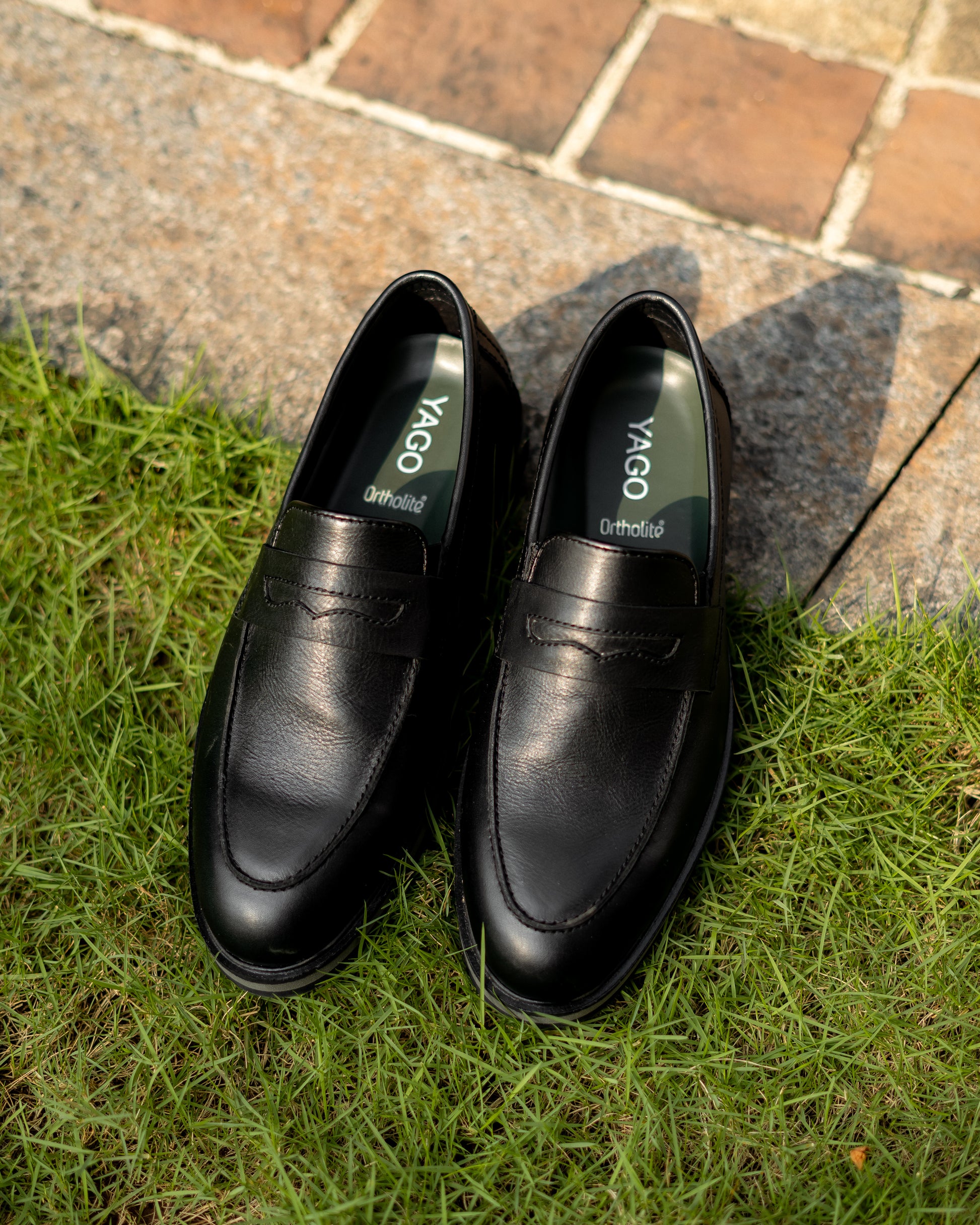 Black leather shoes with 'YAGO' branding on a grassy and stone surface